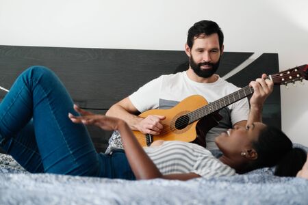 Man Playing Guitar And Woman Singing Song In Bedroomの写真素材