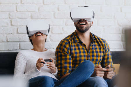 Young Couple Playing Virtual Reality With Headset On Sofaの写真素材