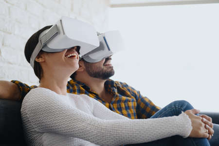Young Couple Playing Virtual Reality With Headset On Sofaの写真素材