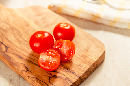 ciligino tomatoes on olive wood cutting board with napkin and cutlery on white tableの写真素材