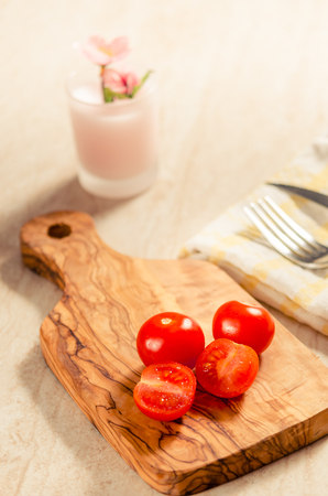 ciligino tomatoes on olive wood cutting board with napkin and cutlery on white tableの写真素材