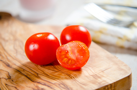 ciligino tomatoes on olive wood cutting board with napkin and cutlery on white tableの写真素材
