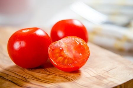 ciligino tomatoes on olive wood cutting board with napkin and cutlery on white tableの写真素材