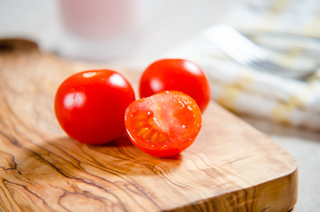 ciligino tomatoes on olive wood cutting board with napkin and cutlery on white tableの写真素材