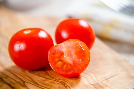 ciligino tomatoes on olive wood cutting board with napkin and cutlery on white tableの写真素材