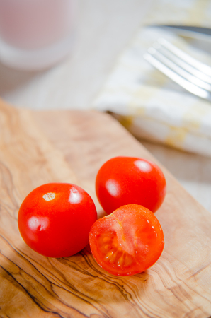 ciligino tomatoes on olive wood cutting board with napkin and cutlery on white tableの写真素材