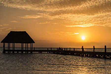 Couple looking at the sun going down on a wooden pier with a hut.の写真素材