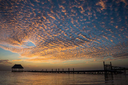 looking at the sun going down on a wooden pier with a hut.の写真素材