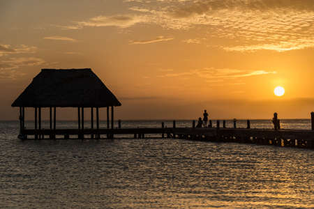 Couple looking at the sun going down on a wooden pier with a hut.の写真素材