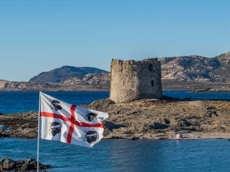 Stintino, Sardinia, Italy - View of the famous La Pelosa Beach with the Sardinian flag and the landmark 16th century Watchtower (Italian: Torre della Pelosa) in the background.のeditorial素材