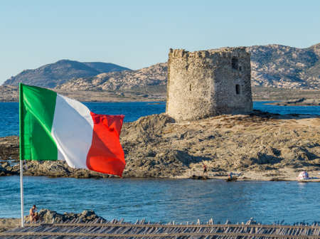 Stintino, Sardinia, Italy - View of the famous La Pelosa Beach with the Italian flag and the landmark 16th century Watchtower (Italian: Torre della Pelosa) in the background.のeditorial素材