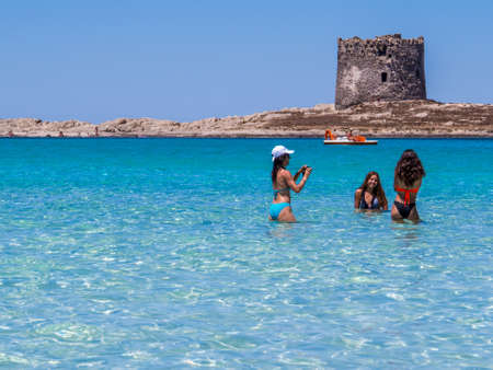 STINTINO, ITALY - JULY 20, 2016: Three girlfriends posing for pictures in the amazing turquoise waters of La Pelosa Beach in Stintino, Sardinia, Italy.のeditorial素材
