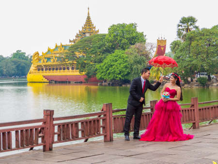 YANGON, MYANMAR - JANUARY 4, 2018: Burmese bride and groom posing for pictures near the  Kandawgyi Lake with the Karaweik Palace in the background.のeditorial素材