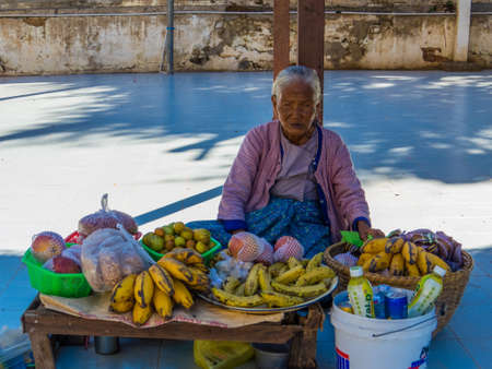 BAGAN, MYANMAR - JANUARY 6, 2018: Old woman selling fruits and eating in front of Manuha Temple.のeditorial素材