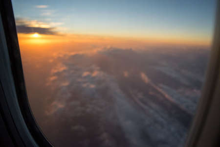 Clouds and sunrise seen from the airplane window, with the window in focus and the background out of...