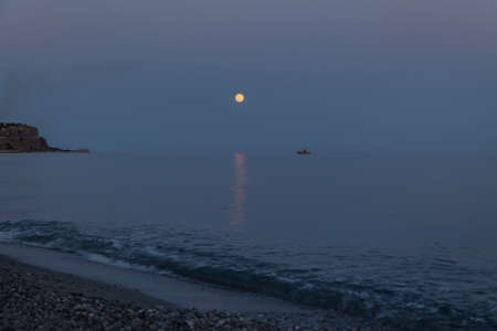 A boat and a rising moon in a Mediterranean beach of Ionian Sea - Bova Marina, Calabria, Italyの写真素材