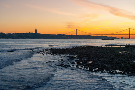 Tagus River (Rio Tejo) at sunset with 25 de Abril Bridge and Sanctuary of Christ the King skyline on...