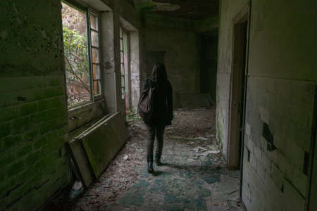 Girl walk in old abandoned building in decay hallway to explore it from back walking with backpackの写真素材