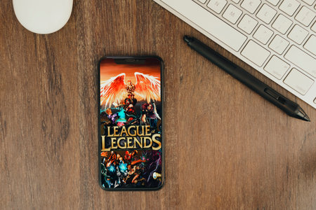 League of Legends game app on the smartphone screen on wooden background with a keyboard and a pen tablet beside it. View from the top. Rio de Janeiro, RJ, Brazil. May 2021.のeditorial素材