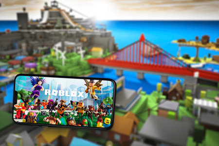 Roblox game app on the smartphone screen with the game screen blurred in the background. Rio de Janeiro, RJ, Brazil. May 2021.のeditorial素材