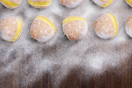 Berlin balls, known as Sonho in Brazil on wooden table with scattered icing sugar. It consists of a fried sweet dough filled with a cream and sugar on top. Top view. Space for text. Selective focus.の写真素材