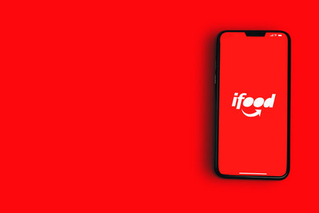 Ifood app on smartphone screen on red background. Ifood logo, online food ordering digital application. Top view. Rio de Janeiro, RJ, Brazil. May, 2021.のeditorial素材