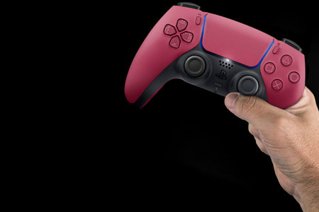 Male hand holding a Playstation 5 Dual Sense Cosmic Red Controller isolated on black background. Rio...