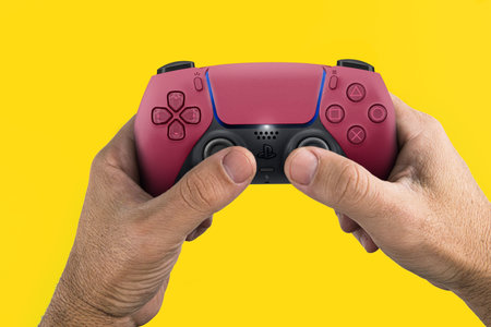 Male hand holding a Playstation 5 Dual Sense Cosmic Red Controller isolated on yellow background. Rio de Janeiro, RJ, Brazil. June 2021.のeditorial素材