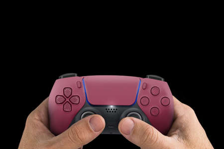 Male hand holding a Next Generation red game controller isolated on black background.