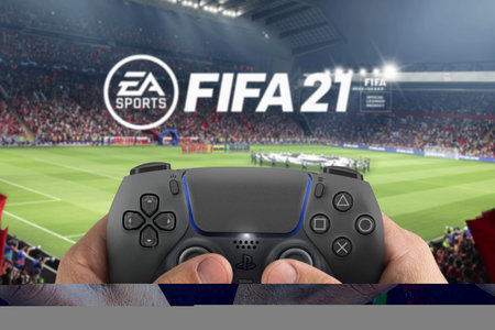 Male hand holding a Playstation 5 Dual Sense Midnight Black Controller with FIFA 21 game blurred in...