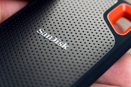 Male hand holding an external Sandisk Extreme SSD Drive isolated on wooden background. Selective focus. Rio de Janeiro, RJ, Brazil. July 2021.のeditorial素材