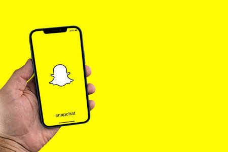 Male hand holding a smartphone with Snapchat app on screen. Yellow background. Rio de Janeiro, RJ,...