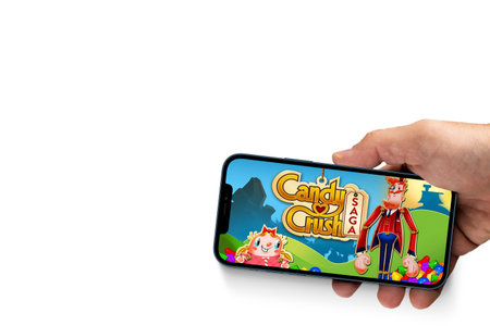 Male hand holding a smartphone with Candy Crush Saga game app on the smartphone screen on white background. Rio de Janeiro, RJ, Brazil. August 2021.のeditorial素材