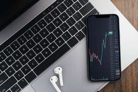 Financial stock market graph on the smartphone screen on wooden background with a computer beside it. Top view. Stock Exchange.の写真素材