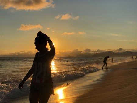 Young girl watching the sunset at Barra da Tijuca beach in Rio de Janeiro, Brazil. Sea with calm waves.の写真素材
