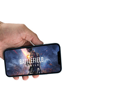 Male hand holding a smartphone with Battlefield Mobile game app on the smartphone screen on white...
