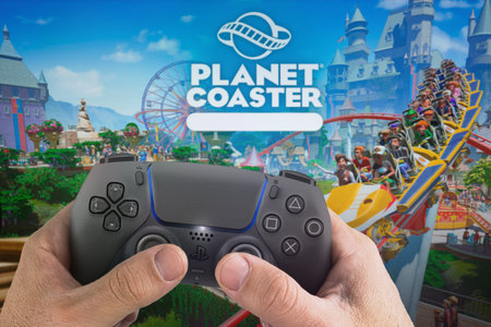 Male hand holding a Playstation 5 Dual Sense Controller with Planet Coaster game blurred in the...