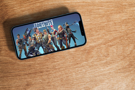 Fortnite mobile game app on smartphone screen with large shadow marked giving the feeling that you are taller on wooden background. Rio de Janeiro, RJ, Brazil. September 2021.のeditorial素材