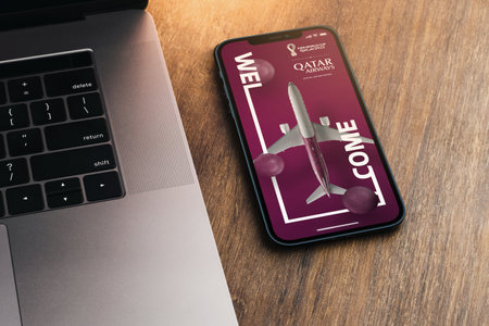 Qatar Airways app on the smartphone screen on wooden background with a computer beside it. Top view. Rio de Janeiro, RJ, Brazil. September 2021.