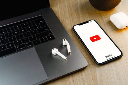 Youtube app on the smartphone screen on wooden background with a computer beside it. Top view. Rio de Janeiro, RJ, Brazil. September 2021.のeditorial素材