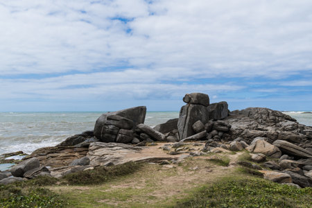 View of the beach of Rio das Ostras in Rio de Janeiro with sunny day, blue sky and some clouds. Strong sea and yellowish sand and lots of rocks.の写真素材