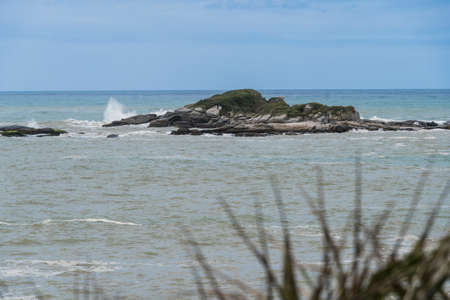 View of the beach of Rio das Ostras in Rio de Janeiro with sunny day, blue sky and some clouds. Strong sea and yellowish sand and lots of rocks.の写真素材