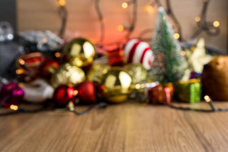 Blurred wooden table background with Christmas baubles. Red, silver and gold balls, gift boxes, lights, panettone, Christmas tree and others to insert something in front in focus.の写真素材