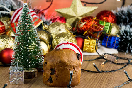 Wooden table with Christmas decorations. Red, silver and gold balls, gift boxes, lights, panettone, Christmas tree and others. Selective focus.の写真素材