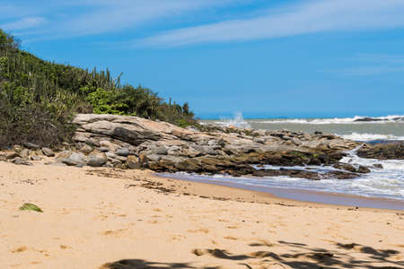 View of the Joana beach in Rio das Ostras in Rio de Janeiro. Sunny day, blue sky. Strong sea and yellowish sand and lots of rocks.の写真素材
