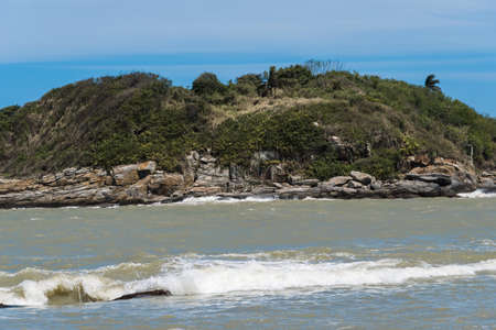 View of the Joana beach in Rio das Ostras in Rio de Janeiro. Sunny day, blue sky. Strong sea and yellowish sand and lots of rocks.の写真素材