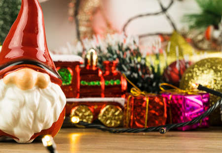 Wooden table with Christmas decorations. Red, silver and gold balls, gift boxes, lights, Santa Claus, Panettone, Christmas tree and others. Selective focus.の写真素材