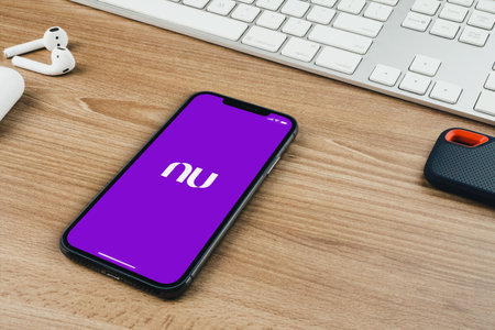Nubank app on the smartphone screen on wooden background with a computer beside it. Office environment. Rio de Janeiro, RJ, Brazil. October 2021.のeditorial素材