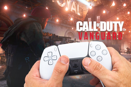 Male hand holding a Playstation 5 Dual Sense Controller with Call of Duty Vanguard game blurred in...
