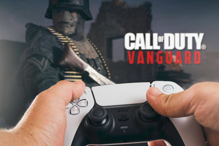 Male hand holding a Playstation 5 Dual Sense Controller with Call of Duty Vanguard game blurred in...
